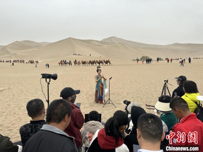 圖為2023年4月底，敦煌大漠“逐舞者”奧楠在鳴沙山月牙泉景區(qū)視頻直播，吸引游人圍觀?！●T志軍 攝
