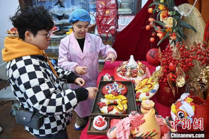 1月25日，隨著春節(jié)臨近，蘭州一花饃店“龍”元素花饃熱銷。圖為工作人員向顧客推薦“龍”元素花饃。九美旦增 攝</p><p>